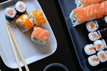 Sushi roll with seafood and soy sauce, wasabi and ginger. Sushi roll with salmon and flying fish caviar on a black table