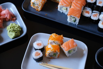Sushi roll with seafood and soy sauce, wasabi and ginger. Sushi roll with salmon and flying fish caviar on a black table