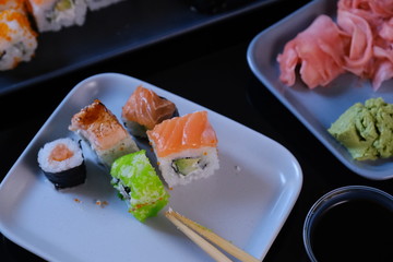 Sushi roll with seafood and soy sauce, wasabi and ginger. Sushi roll with salmon and flying fish caviar on a black table