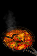 Traditional homemade spicy turkey stew with vegetables and paprika, indoor, process of cooking in a pan at black background, closeup, details