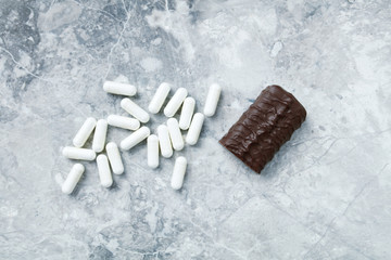 High Protein bar and Arginine capsules.  Bodybuilding food supplements on bright stone background. Top view. Copy space. 