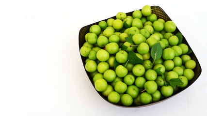 green plums on white ground, fresh plums, sour plums in a container, green and sour plums,