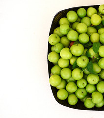 green plums on white ground, fresh plums, sour plums in a container, green and sour plums,