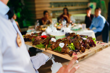 Meat ribs on a tray with liquid nitrogen. The waiter serves food in front of the guests in the restaurant. Delicious meat dish with non-standard serving