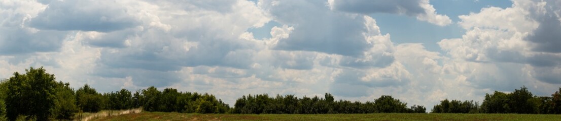 Obraz premium Fields and forests of Bulgaria before the rain. Cumuliform cloudscape on blue sky. The terrain in southern Europe. Fantastic skies on the planet earth. The sun is hidden. Panorama.