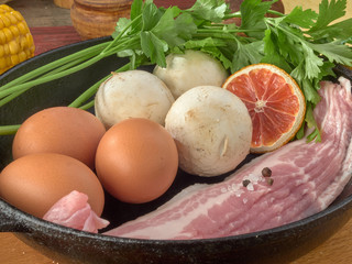 Eco chicken eggs.Champignons.Bacon of pork belly are fried in a black cast iron skillet.On wooden background 