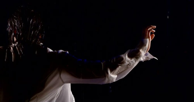 female dancer is moving hand standing back to camera in dark studio with water flows falling
