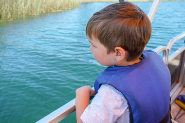 Fototapeta na wymiar Cute little boy enjoying ride on a small boat. Little kid in the bow of a boat with his blue life jacket having fun. Travel adventure family vacation.