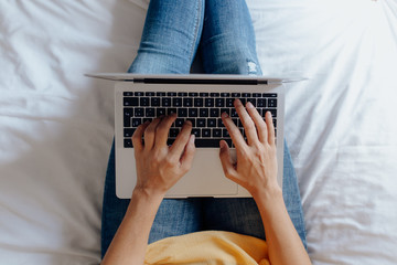 Unrecognizable woman sitting on the bed typing on the laptop