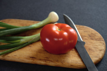 Green onions and tomato on a cutting board with a knife