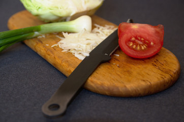Chopped cabbage, piece of tomato and green onion on a cutting board with a knife