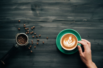 Female hands holding a cup of coffee Latte art over wooden table, top view