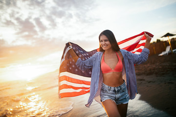 Cheerful happy woman outdoors on the beach holding USA flag having fun.