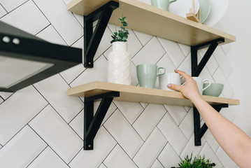 A womans hand taking a cup from a shelf on a white tiled kitchen wall