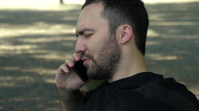 Handsome young man akes a call in a park.