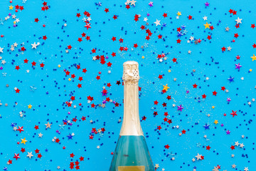 Champagne bottle with colorful party streamers for celebration on blue background top view pattern