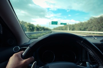 Inside view, hand of a driver on steering wheel of a car with empty asphalt road background....