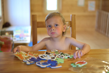 Happy cute little boy love playing with toys. Adorable blond-haired little child. The kid is sitting at the table and playing Board games.