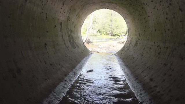 Big culvert under the highway. The video operator is on the water in the pipe and shoots a movie