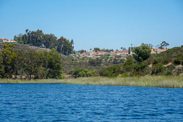 Fototapeta na wymiar Big lake with blue water, trees and native wetland plants and villa on the cliff with blue sky. Miramar reservoir in the Scripps Miramar Ranch community, San Diego, California