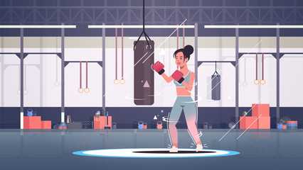Obraz premium woman boxer doing exercises with punching bag making direct hit in red boxing gloves sportswoman fighter training workout healthy lifestyle concept modern gym sport club interior horizontal