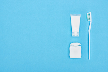 top view of toothbrush and toothpaste near dental floss isolated on blue