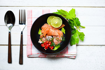 Salmon Salad / Fish salmon fillet on bolw and spoon fork on dining table background - Close up of raw salmon sashimi seafood with chilli lime herbs and spices , top view