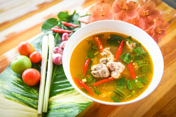 Pork rib spicy soup - pork bone with hot and sour soup bowl with fresh vegetables Tom Yum thai herbs and spices ingredients with chilli lemon on wooden background , Thai Food Asian