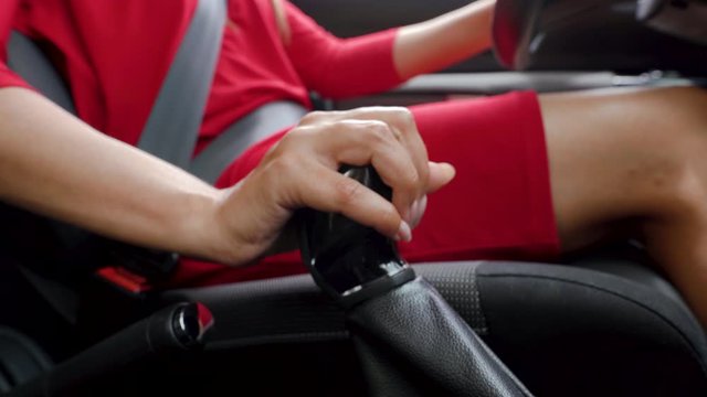 Close-up of woman driver in red dress shifts gears while driving