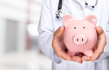 Doctor with Stethoscope Holding Piggy Bank