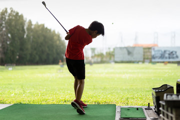 Young asian boy is practicing his golf swing at the golf driving range.