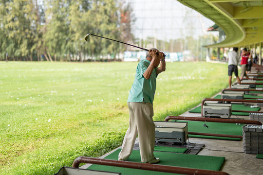 Senior man exercise practicing his golf swing at golf driving range.