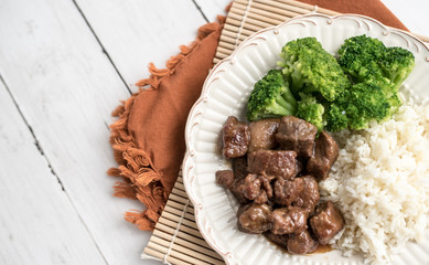 Beef and broccoli Chinese dish over white rice. on a light wood background table