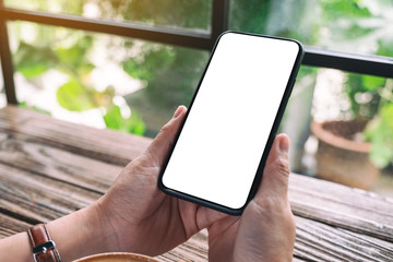 Mockup image of hands holding black mobile phone with blank desktop screen on wooden table