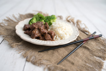 Beef and broccoli Chinese dish over white rice. on a light wood background table