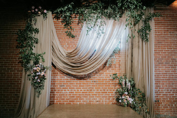 Wedding ceremony alter with hanging fabric, greenery, and flowers, brick background