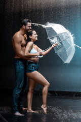 happy bearded man hugging attractive girlfriend holding umbrella near splash of water on black