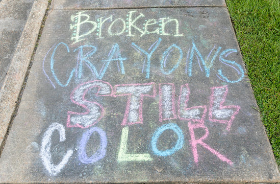 the words "Broken Crayons still color" written with sidewalk chalk on gray concrete pavement background