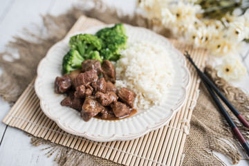 Beef and broccoli Chinese dish over white rice. on a light wood background table