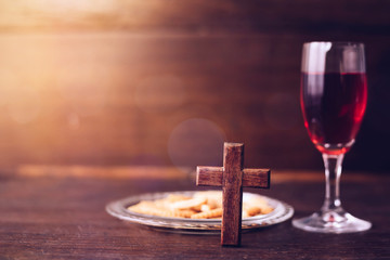Close up of wooden cross with a cup of Grape juice and piece of bread on wooden table for communion, Christian concept for reminder of Jesus who died for human on the cross, copy space