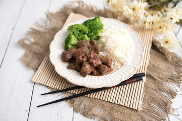Beef and broccoli Chinese dish over white rice. on a light wood background table