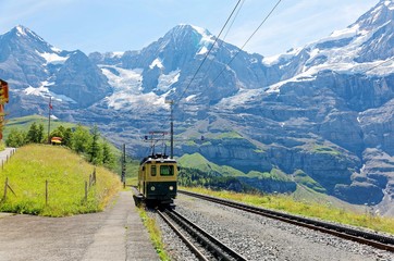 Fototapeta na wymiar A cog wheel train traveling on the mountain Railway from Wengen to Kleine Scheidegg station with majestic Swiss Alps ( Eiger, Monch, Jungfrau ) in background, in Bernese Highlands, Switzerland, Europe