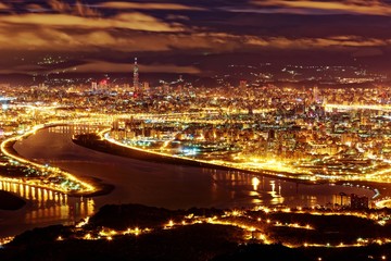 Fototapeta na wymiar Aerial panorama of Taipei City in a blue gloomy night, with view of Guandu plain, Tamsui River, downtown area and landmark tower in XinYi District, in evening twilight