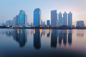 Beautiful city skyline of Bangkok at dawn with lakeside skyscrapers and reflections ~ Morning view of glass curtain walled buildings reflected on smooth lake water in Benjakiti Park, Bangkok Thailand