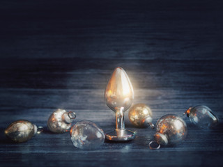 Shining Christmas decorations and a metal butt plug (sex toy) are on a black wooden background. Image for a sex shop for Christmas and New Year.
