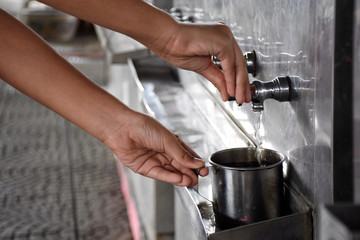 Fototapeta na wymiar Women's hands are dropping water from a stainless steel dispenser, put in an old and dirty stainless steel cup