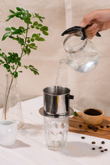Drip, Brewing, pouring water over ground coffee contained in Vietnamese Phin Filter on dark wooden board. Selective Focus.