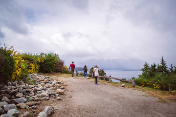 Landscape with three people/tourists walking to a lake lookout, with trees and rocks, with mountains behind, in Villa La Angostura, Patagonia Argentina.