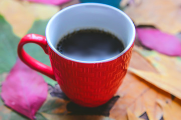 colored cups with hot black coffee on a background of autumn leaves on a wooden table