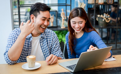 Fototapeta premium Asian couple in blue shirt drinking coffee talking and working with computer laptop smile and happy mood in coffee shop cafe